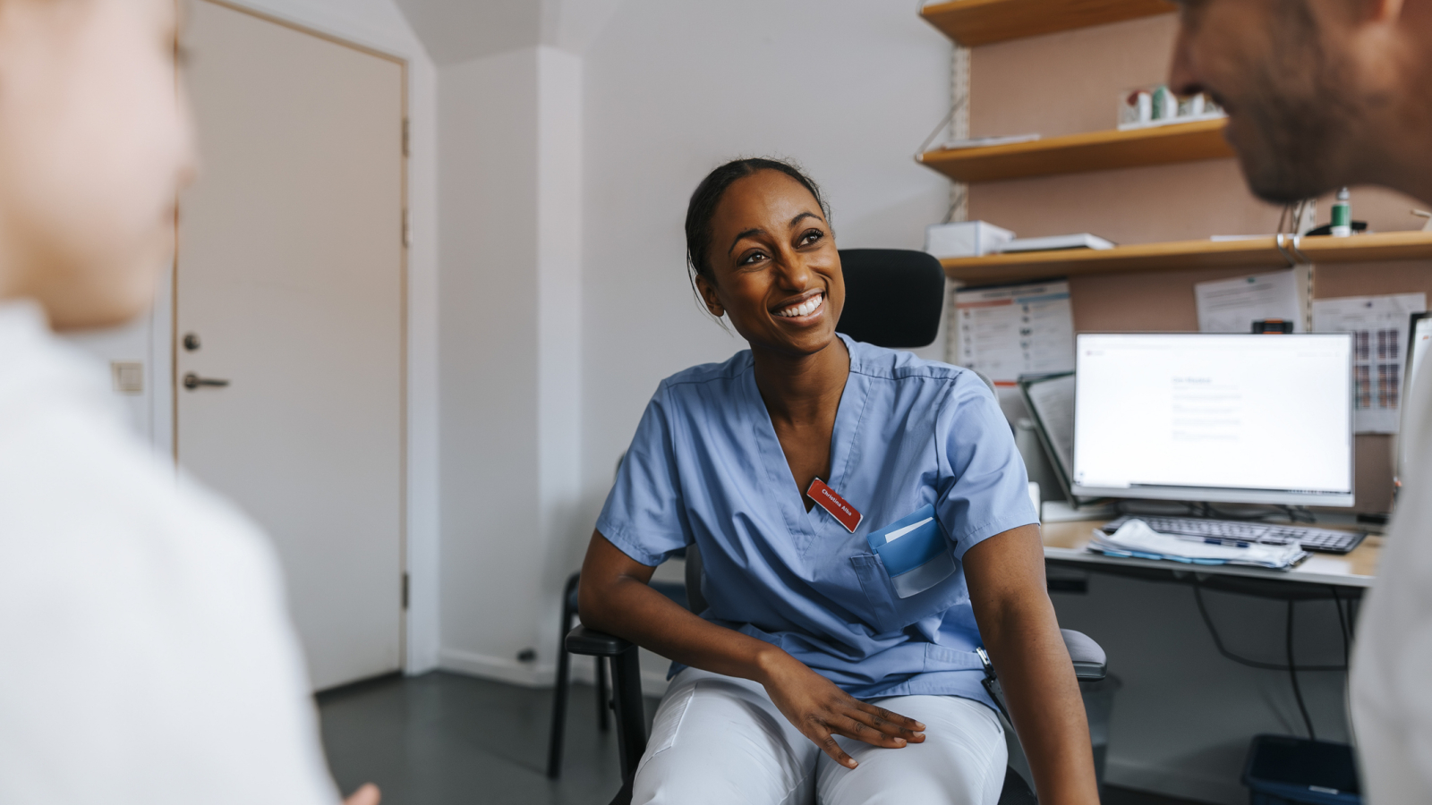 Smiling female healthcare worker in scrubs discussing with father and daughter while sitting in examination room