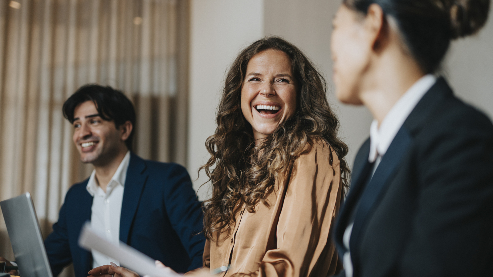 Happy mature businesswoman sitting amidst male and female colleague at office