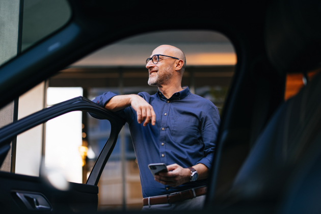 Confident Businessman Standing by Car with Smartphone in City