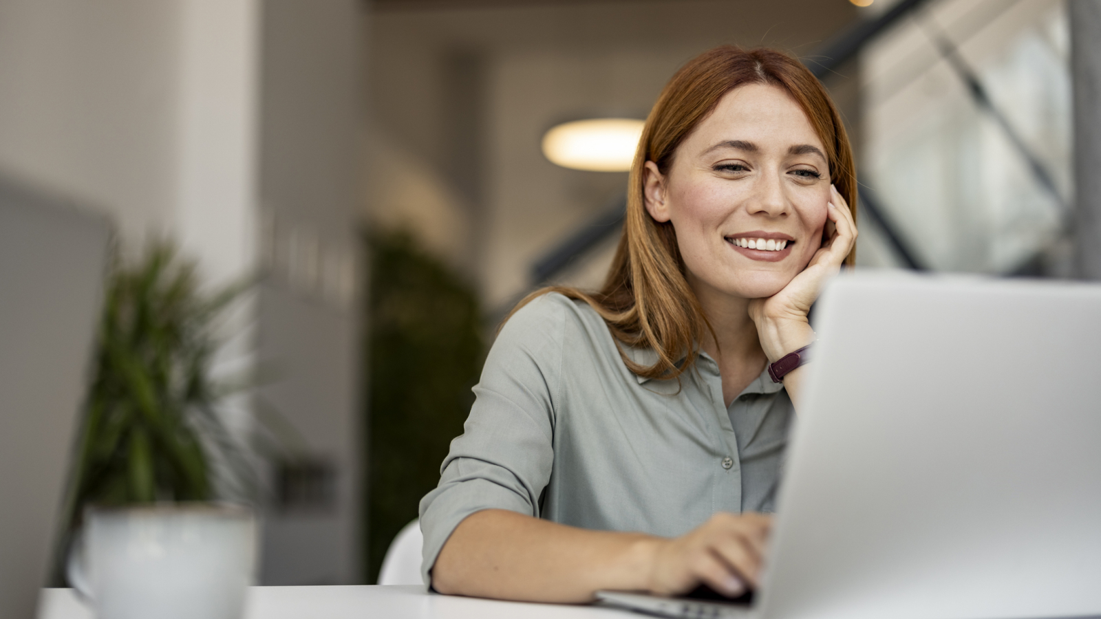 Smiling Woman Working Remotely on Laptop in Modern Workspace