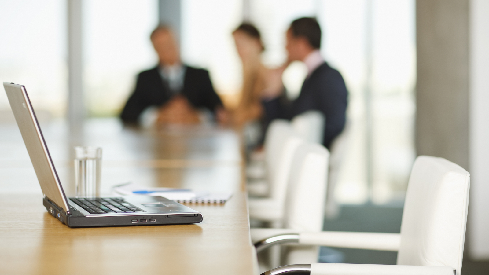 Laptop on conference room table with business people in background