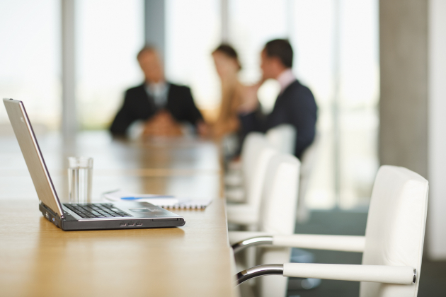 Laptop on conference room table with business people in background