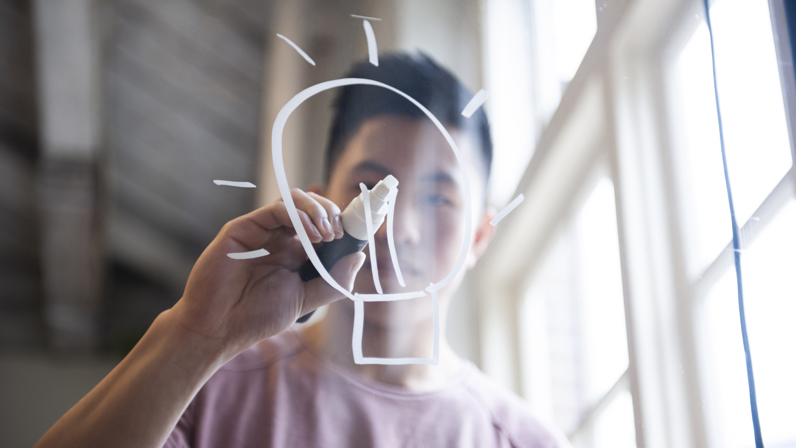 Ideas! Fifteen year old boy drawing a lightbulb on glass with a chalk marker