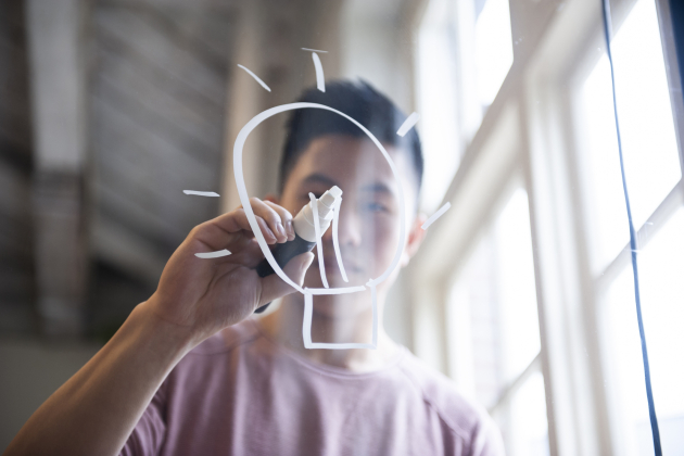 Ideas! Fifteen year old boy drawing a lightbulb on glass with a chalk marker