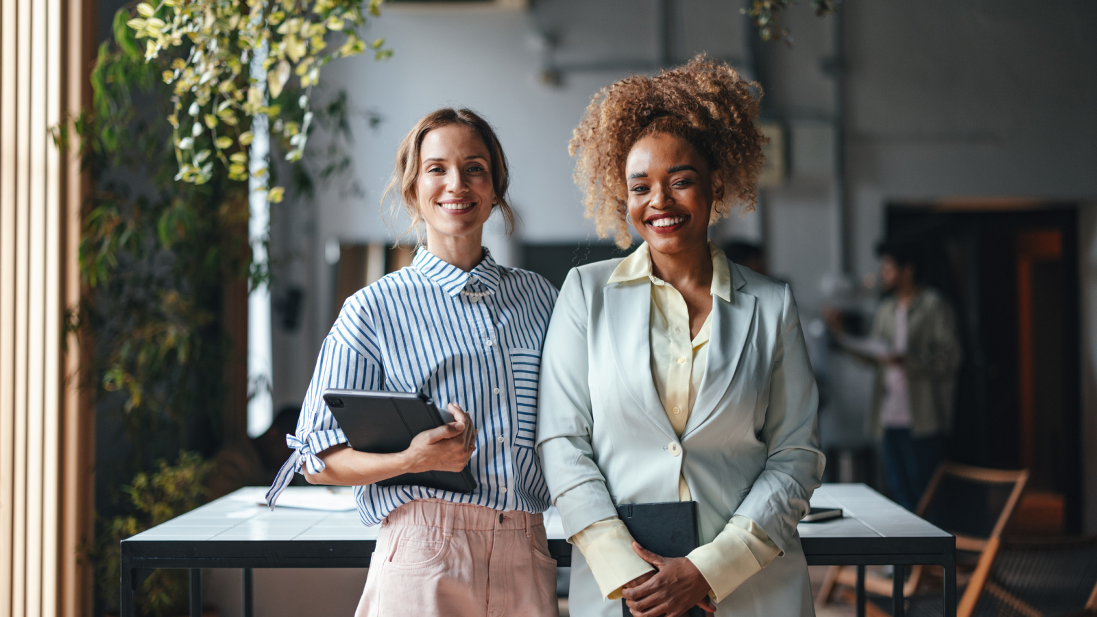 Two Happy Beautiful Blonde Businesswomen Looking At Camera While Standing In The Office