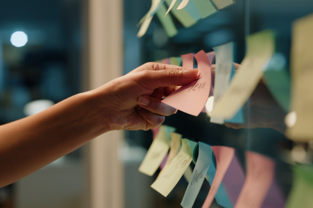 Hand, business and sticky note with planning, ideas and creativity for novel and schedule for writing. Person, closeup or author with brainstorming or research for project, paper or story development