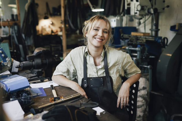 Portrait of smiling female craftsperson sitting on chair at workshop