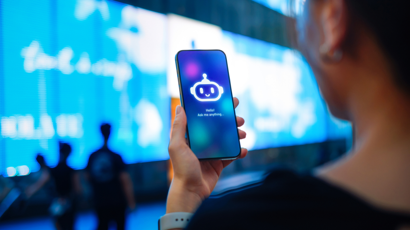 Asian woman standing against illuminated digital display on the street in city, speaking to virtual assistant, chatting AI chatbot app on smartphone. Concept of VR and AR technologies. Metaverse and futuristic data. People, AI, innovation and technology