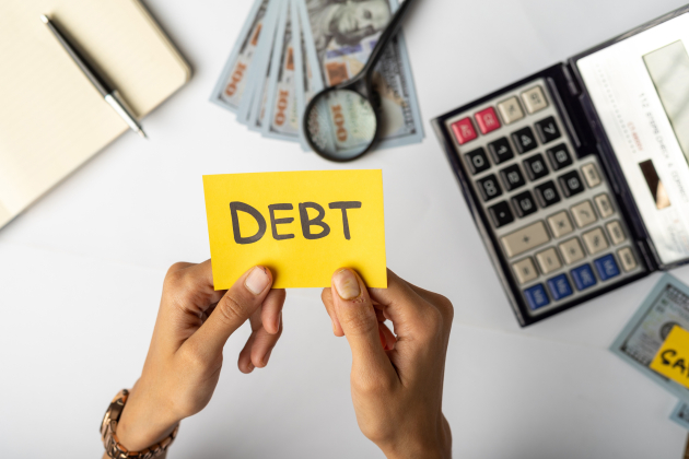 Hands Holding “DEBT” Label with Financial Tools and Money