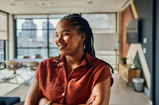 Confident computer programmer smiling and crossing arms in modern office