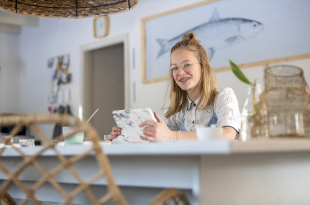 Portrait of blonde attractive young woman on her tablet at the kitchen table
