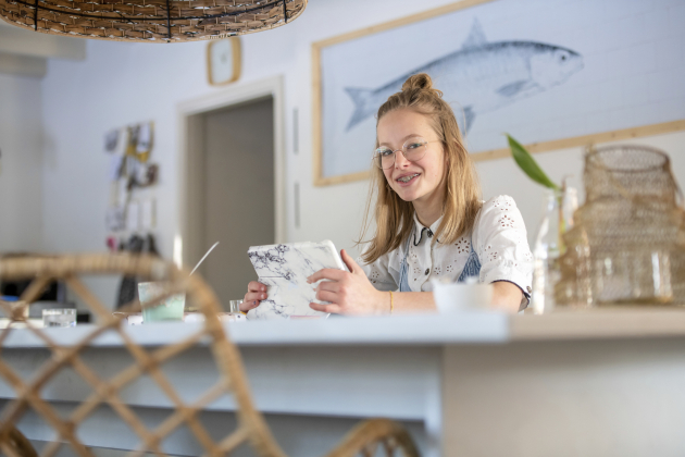 Portrait of blonde attractive young woman on her tablet at the kitchen table