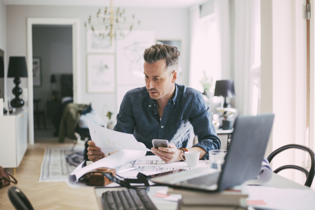 Male architect sitting at workplace reading blueprint at home