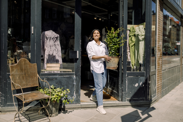 Smiling young female entrepreneur holding plant while walking out of store