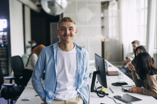 Portrait of smiling male entrepreneur leaning on desk at office