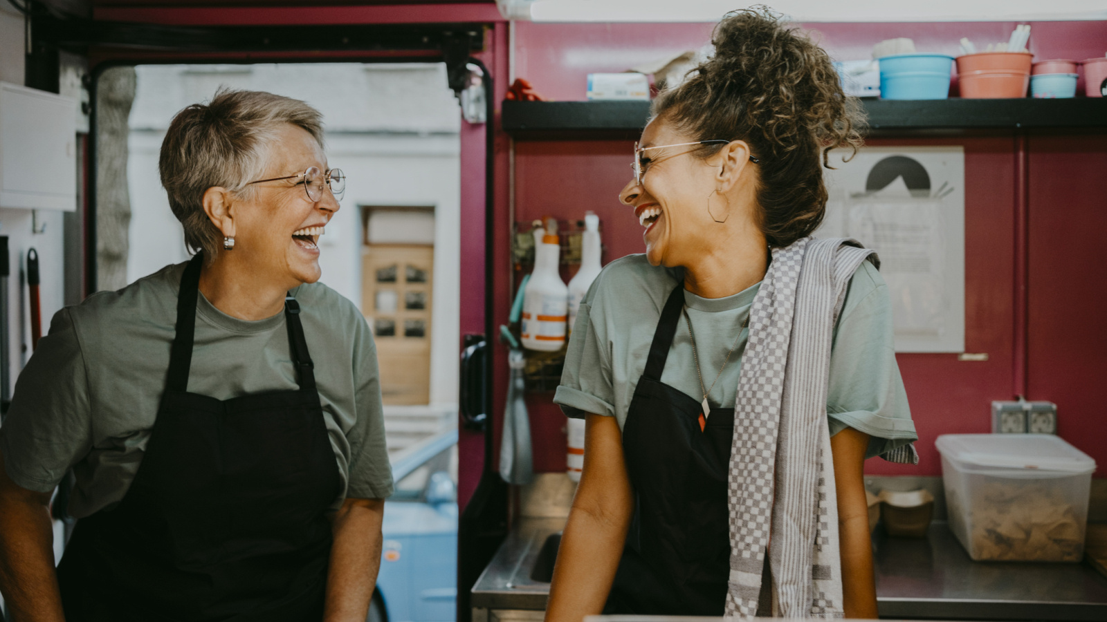 Female owner and coworker laughing in food truck kitchen