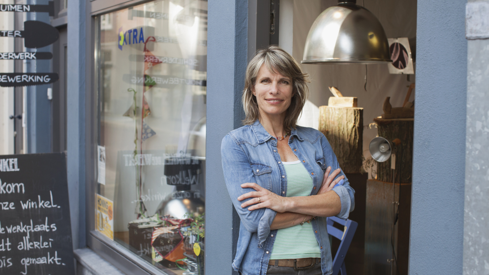 Woman in shop doorway, arms crossed looking at camera smiling