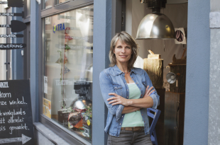Woman in shop doorway, arms crossed looking at camera smiling