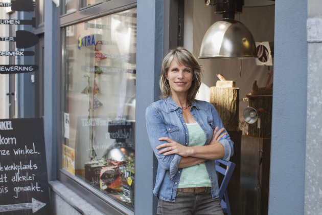 Woman in shop doorway, arms crossed looking at camera smiling