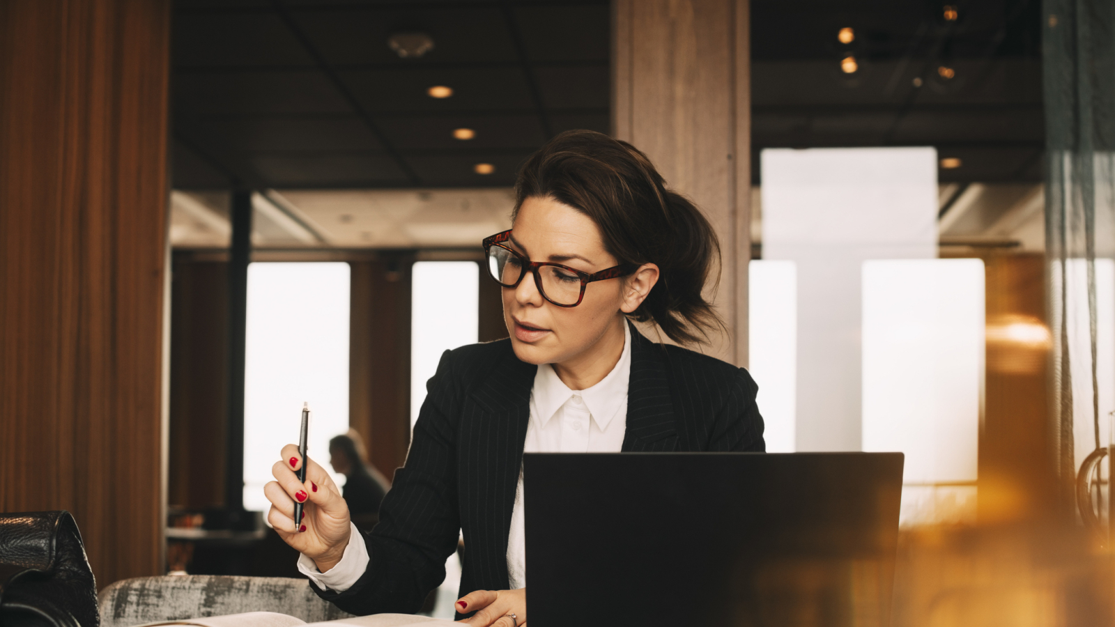 Female lawyer with laptop concentrating while reading book at office