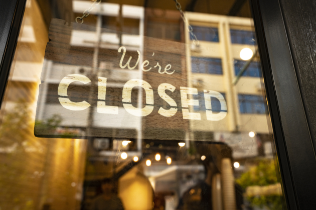 Closed sign hanging in business window by a string – crooked with glob of glue also attaching it to window