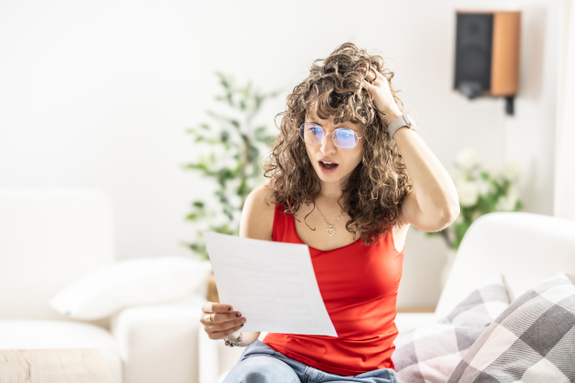 Shocked young woman reading a letter she received from a lawyer, office or utility bill.