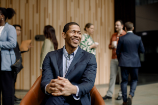 Smiling male entrepreneur sitting on chair with hands intertwined at convention center