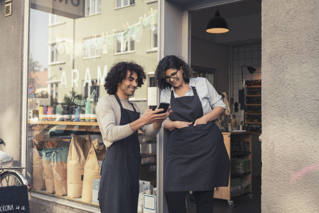 Cheerful male and female owners sharing smart phone at doorway