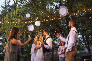 Guests with smartphones taking photo of bride and groom at wedding reception outside.