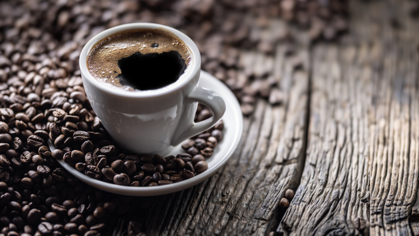 Cup of black coffee with coffee beans on old wooden table