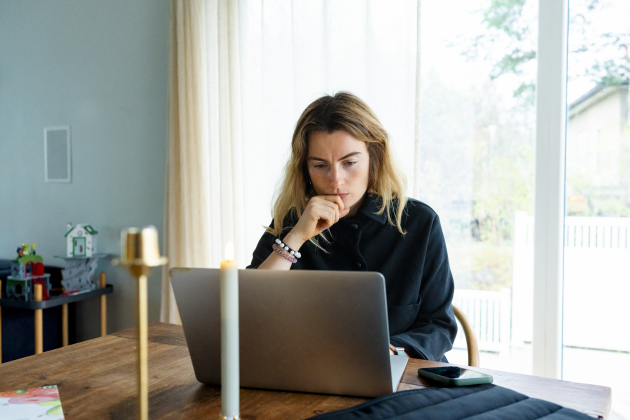 Thoughtful freelancer with hand on chin working on laptop at home office