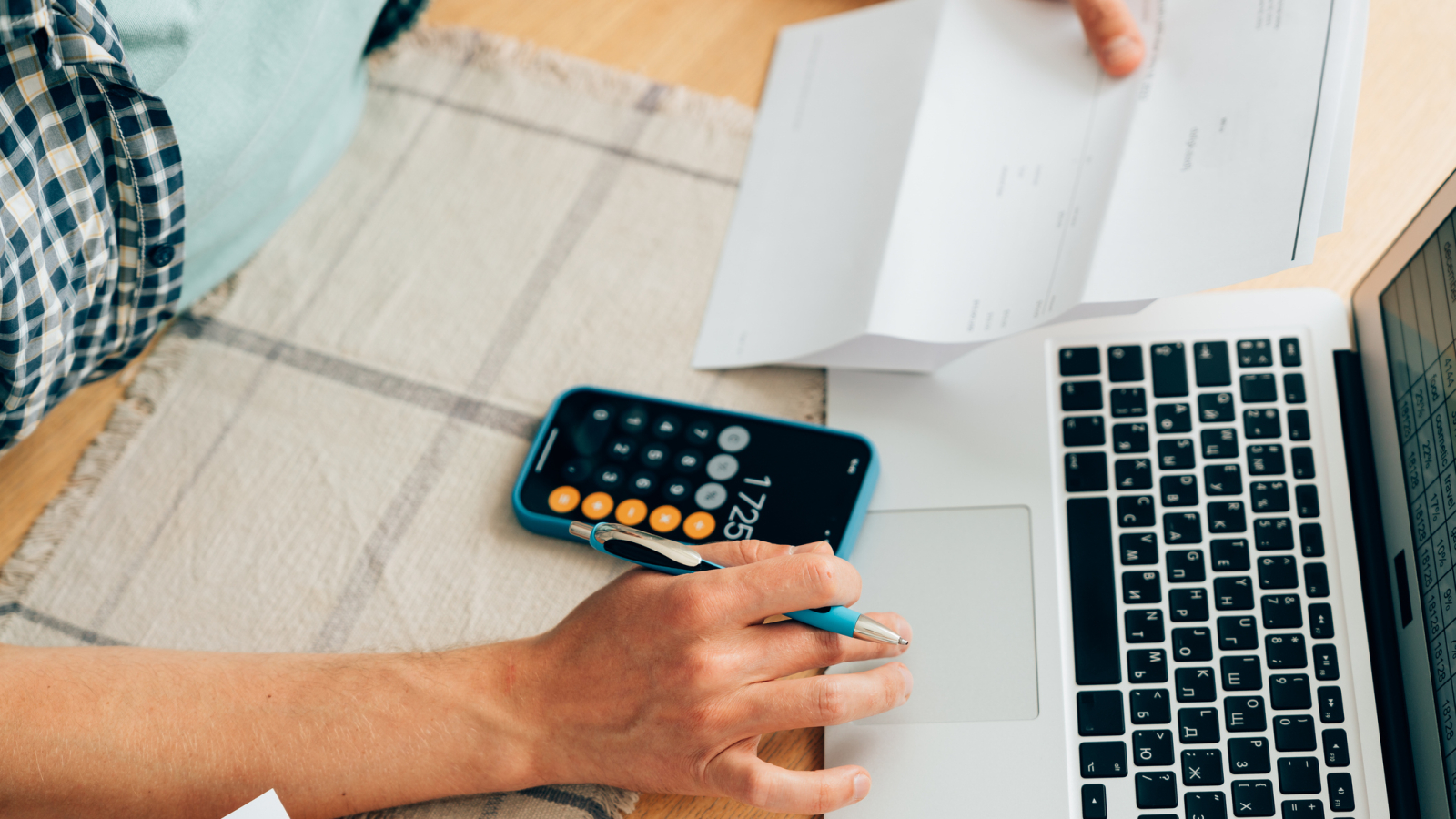 Unrecognizable person counting expenses on calculator in mobile phone app, checking her energy bills at home. Budget management, price increases, inflation, rise in price of products and utilities. View from above, managing home finances