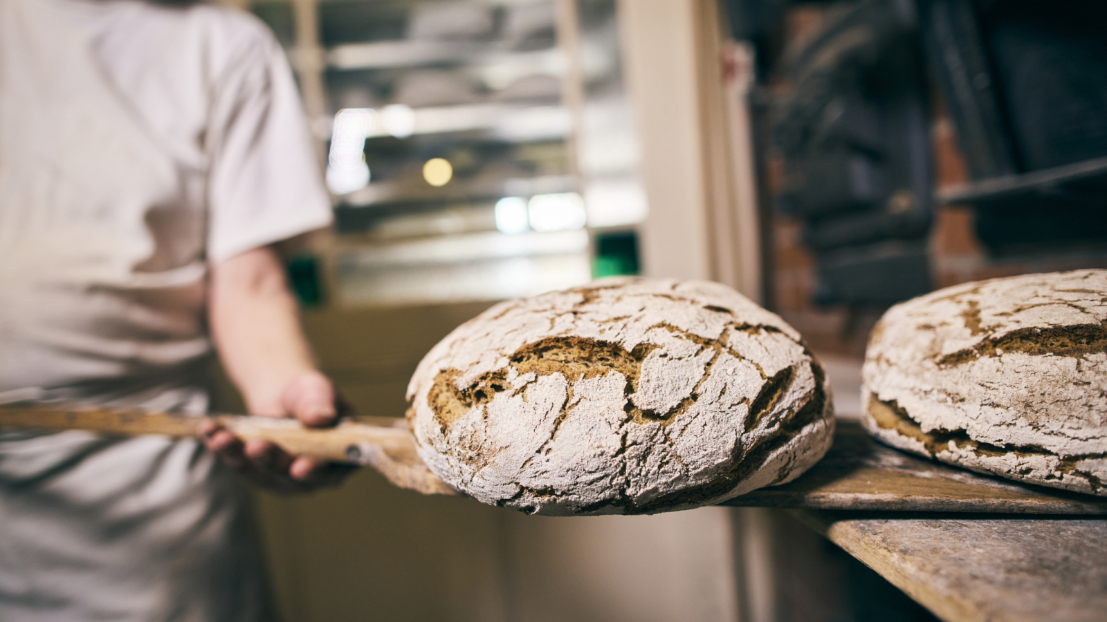 Baker putting bread into oven in his bakery