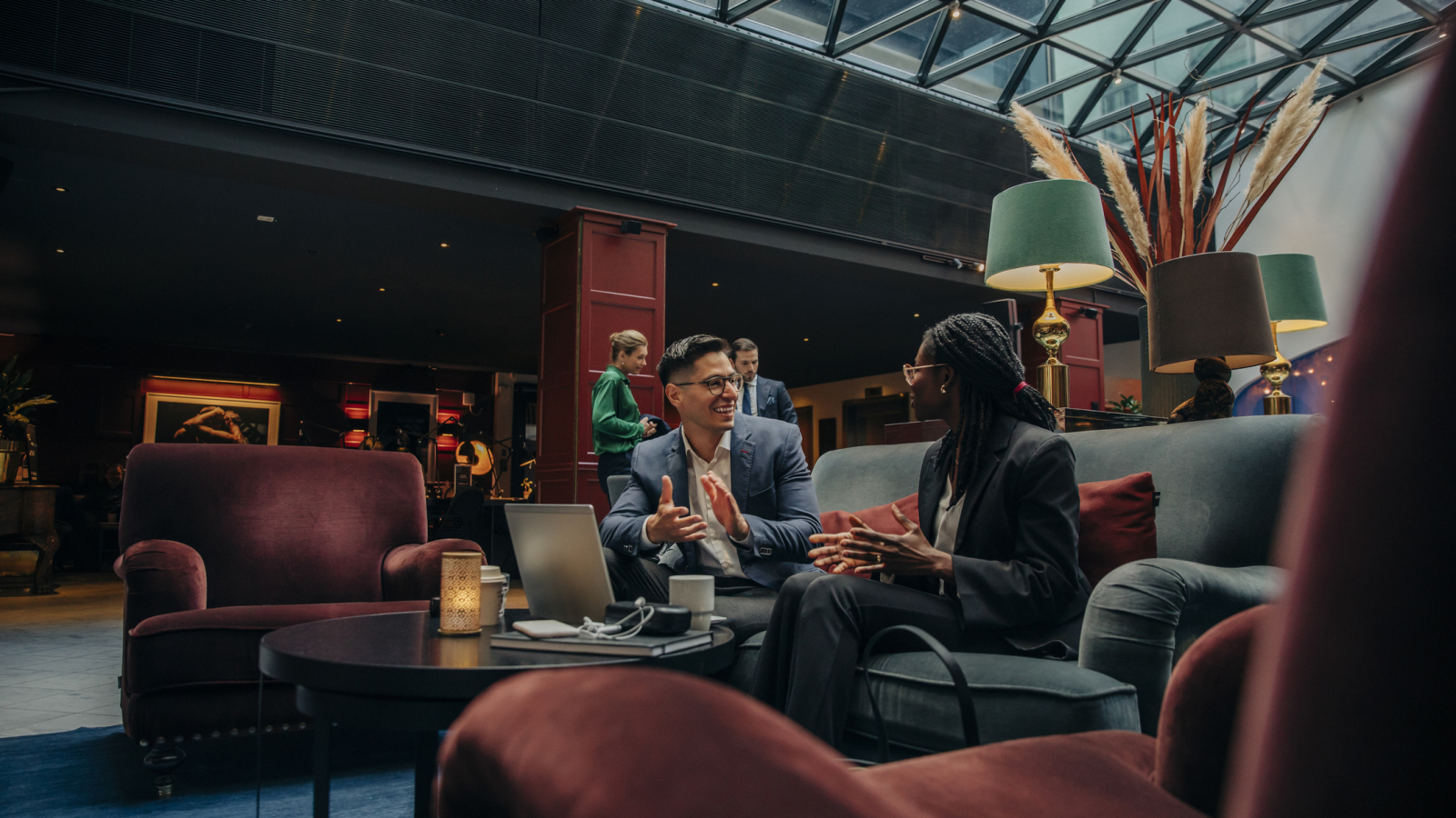 Smiling male professional discussing with female colleague sitting in hotel lounge