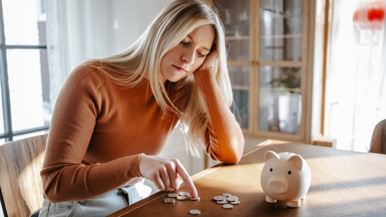 Woman contemplating savings with piggy bank and coins at home