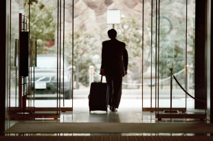 Businessman leaving lobby with luggage, rear view