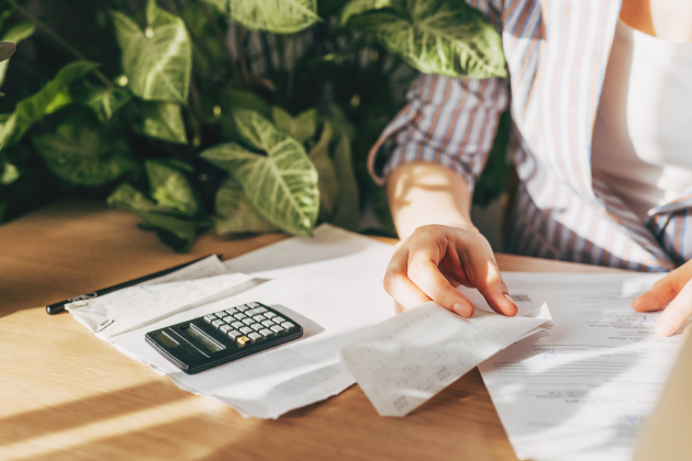 Top view close up woman calculating bills, money, loan or rent payments, using laptop, online banking service, sitting at table, female holding receipt, planning budget, managing expenses, finances